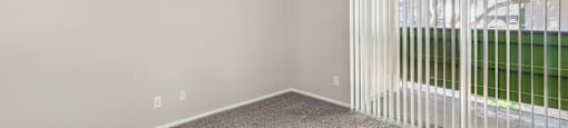 an empty living room with a large window and white blinds